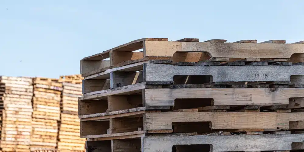 Top stack of used wooden pallets of varying colors with more used pallets in the background