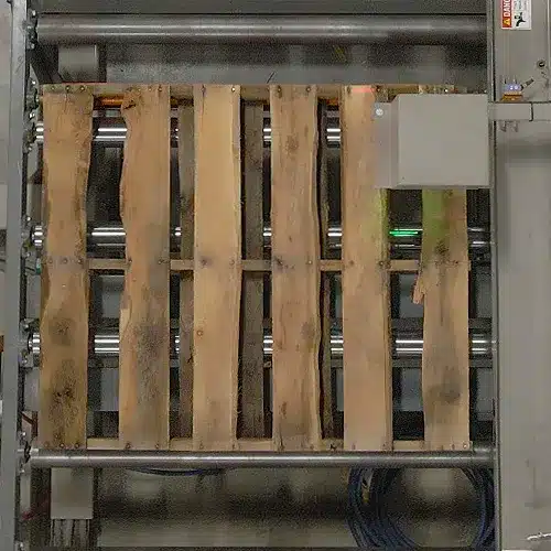 Top view of a used wooden pallet on a conveyor being scanned by a box.