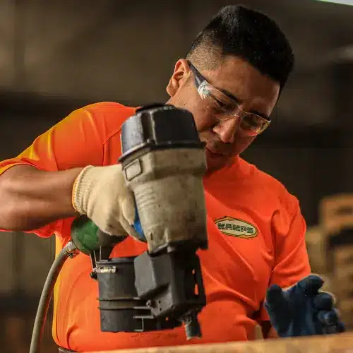 Man holding a nail gun and wearing safety glasses repairing a wooden pallet