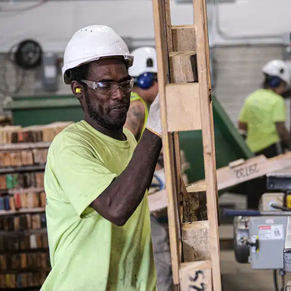 Man wearing PPE carrying wooden block pallet