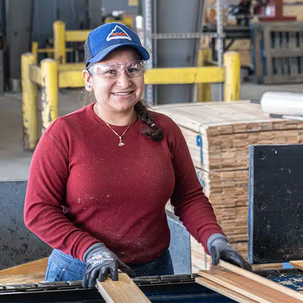 Woman wearing safety glasses and gloves handling lumber on assembly line